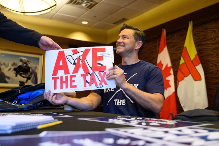 A dark-haired man smiles while holding an Axe the Tax sign. A dark-haired man smiles while holding an Axe the Tax sign.