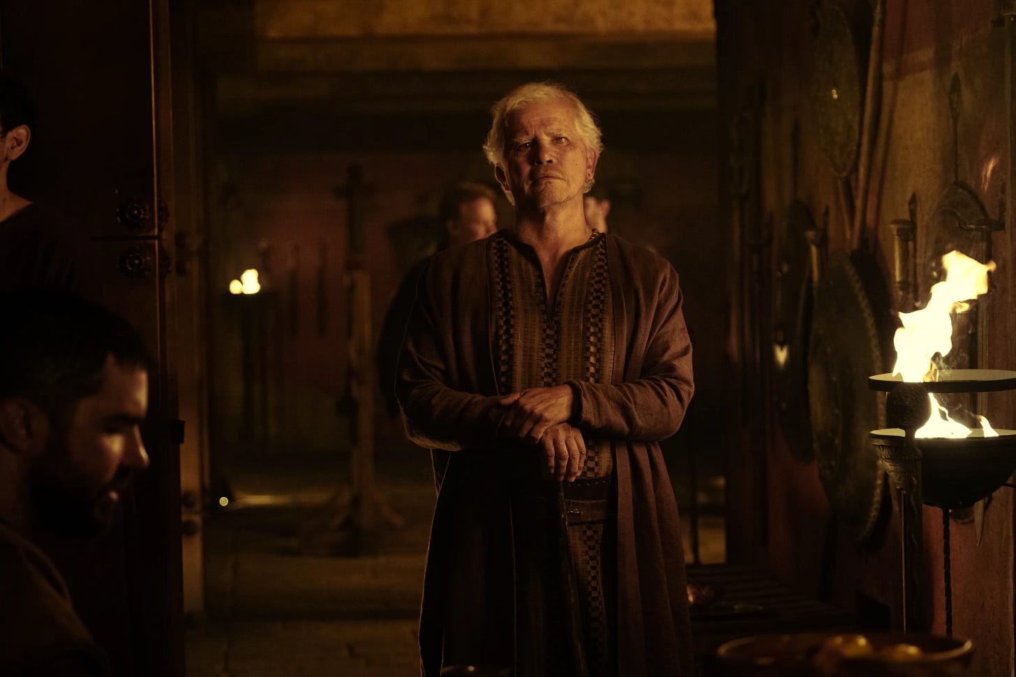 movie still from The Odyssey. John Leguizamo as Eumaeus stands in a dimly lit hall.