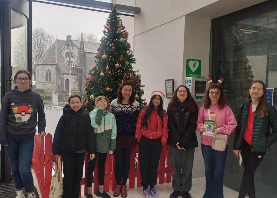 A group of children and a librarian stand in front of a christmas tree