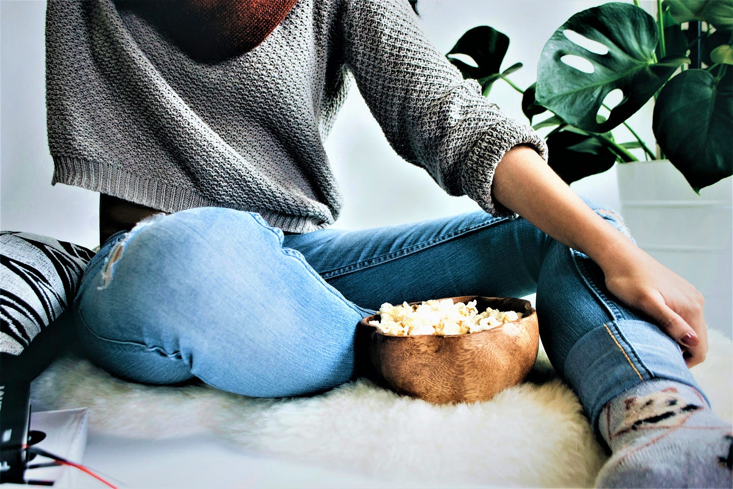 girl wearing grey sweater and blue jeans eating bowl of popcorn