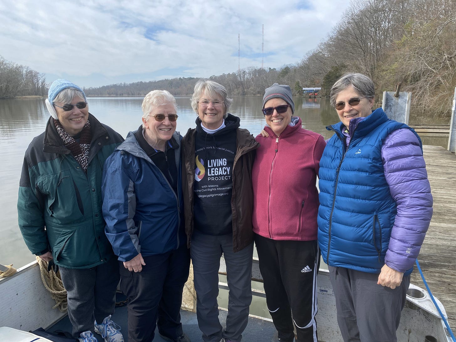 Five older women in jackets standing on a boat in a river