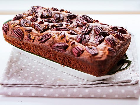 Homemade banana bread topped with pecans, shown whole and sliced to reveal a moist, tender crumb, styled with ripe bananas on a neutral linen background.