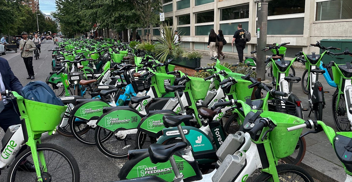 Dozens, maybe a hundred, Lime bikes parked in the road on a quiet street.