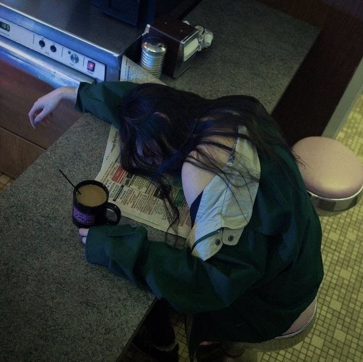 This may contain: a woman sitting on the floor with her head down and holding a cup of coffee