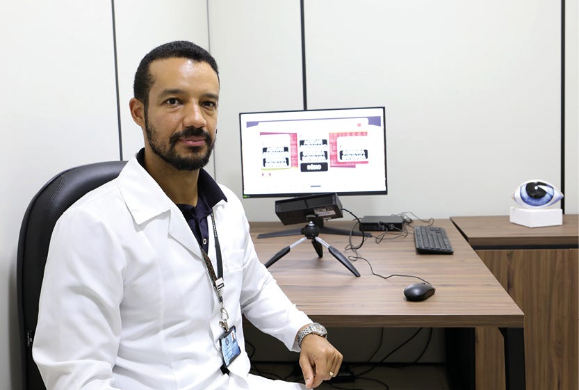 Profissional de saúde vestindo jaleco branco sentado em uma mesa de escritório com computador, microfone e equipamentos de trabalho ao fundo. Profissional de saúde vestindo jaleco branco sentado em uma mesa de escritório com computador, microfone e equipamentos de trabalho ao fundo.