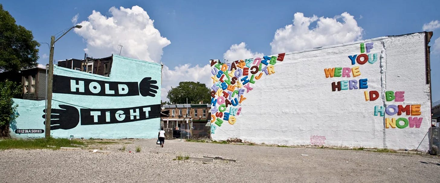 two philadelphia murals on the side of neighbouring buildings, one saying "hold tight" and one saying "if you were here id be home now"