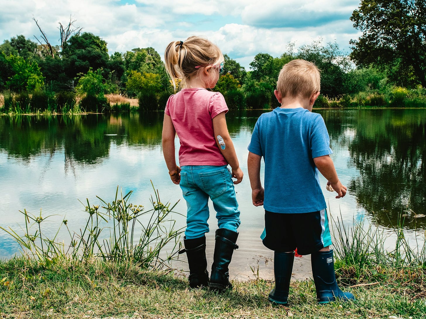 A girl and boy standing next to a pond. A girl and boy standing next to a pond.