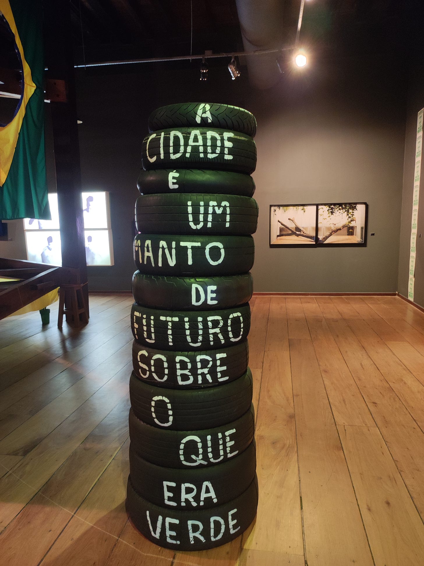 pneus empilhados com a frase escrita em tinta branca "A cidade é um manto de futuro sobre o que era verde"