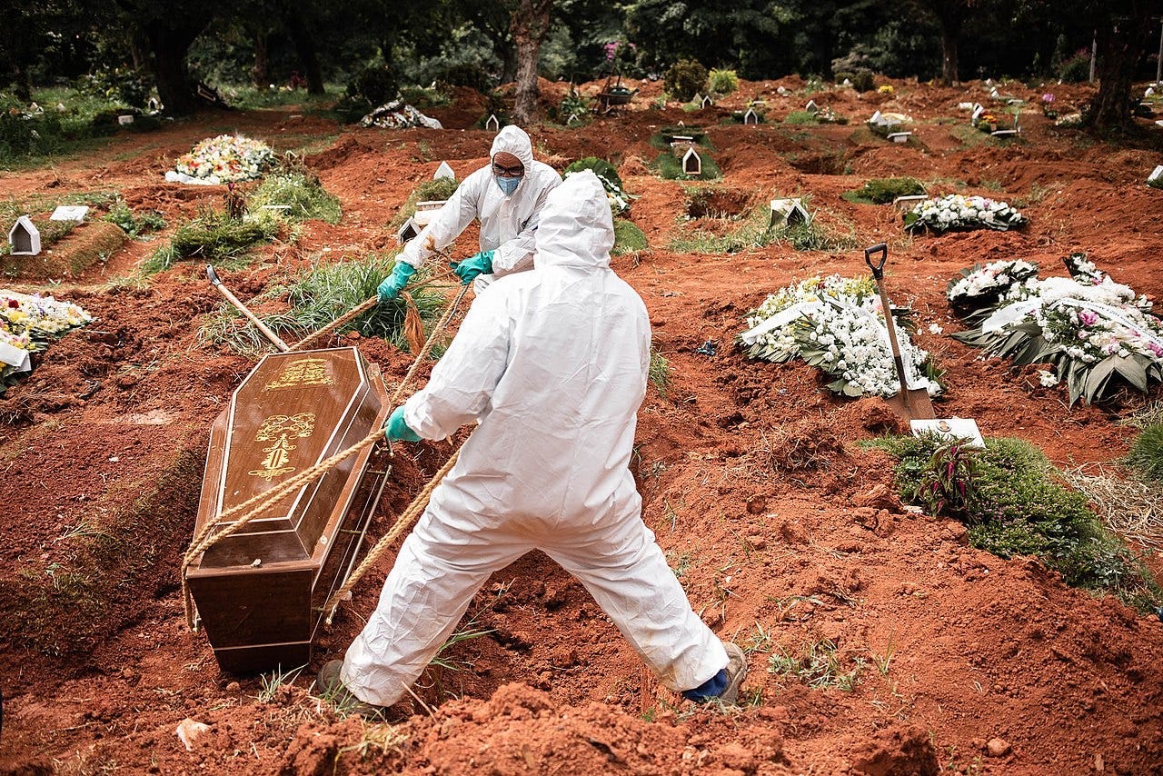 Gravediggers in hazmat suits drag a casket in the cemetery of Vila Alpina in eastern São Paulo. Numerous fresh plots dot the landscape around them.