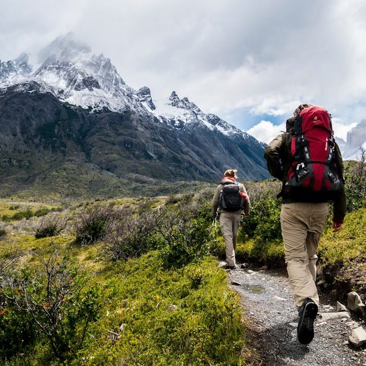 two person walking towards mountain covered with snow two person walking towards mountain covered with snow