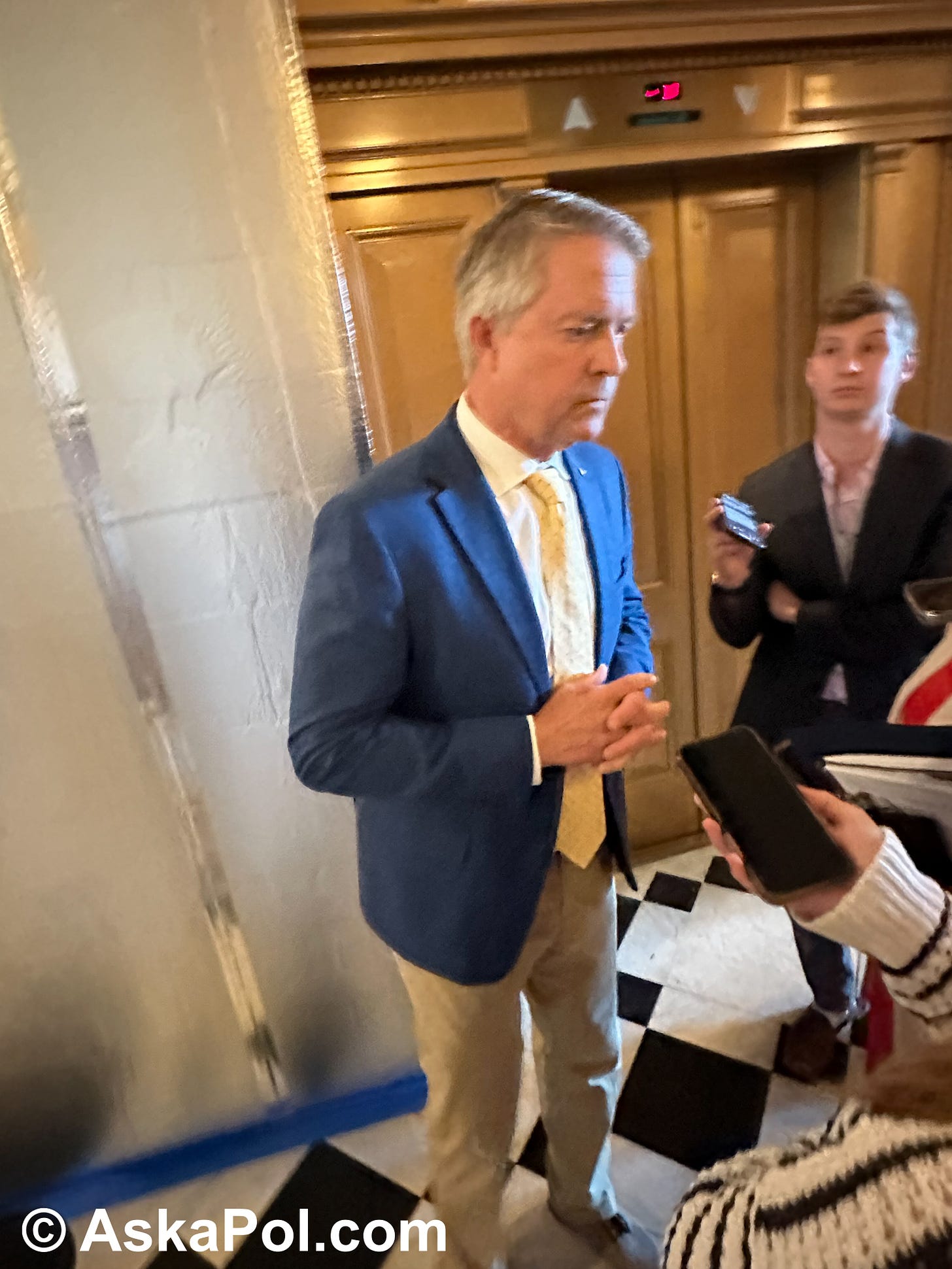 A Senator in a suit and tie answers reporters' questions near elavators and some construction. Photo Matt Laslo for © www.askapolpolitics.com A Senator in a suit and tie answers reporters' questions near elavators and some construction. Photo Matt Laslo for © www.askapolpolitics.com