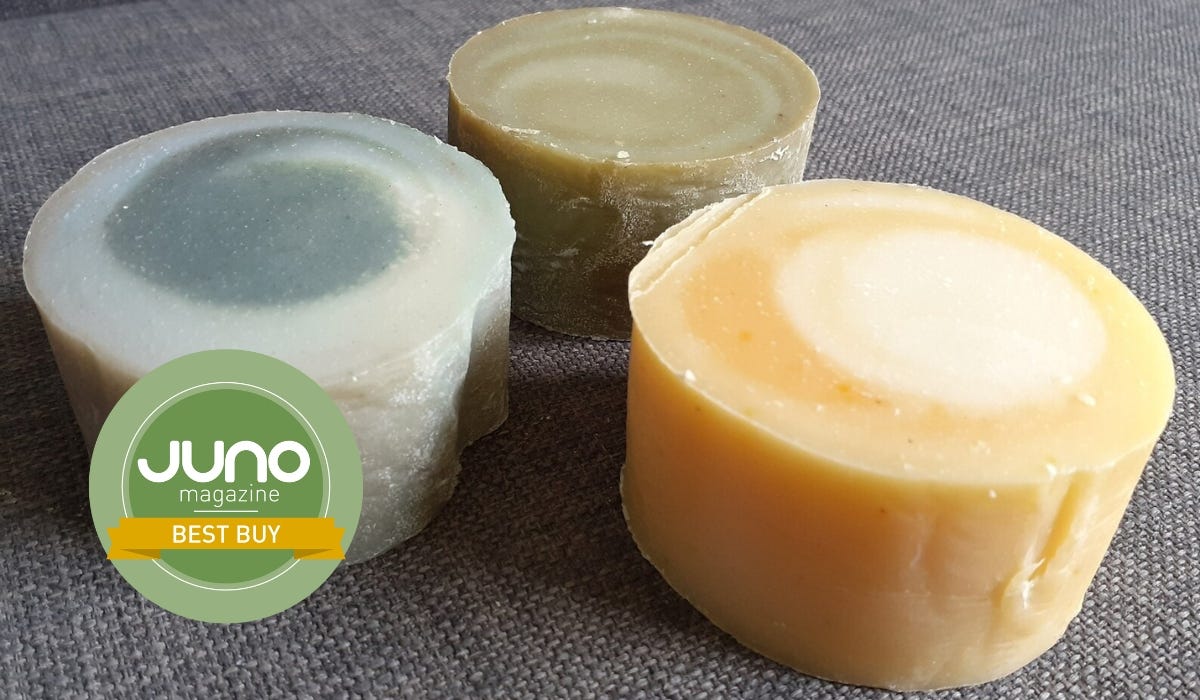 Three round bars of natural soap in green, yellow, and beige, with a "Best Buy" badge from Juno magazine displayed prominently.