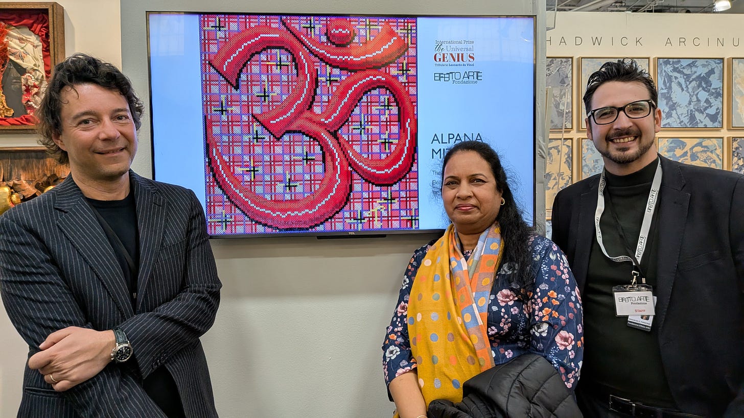 Artist Alpana Mittal, middle-aged woman of Indian background, in stylish multicolored garbs, stands in front of screen showing her beadwork featuring Om symbol, in between two representatives of Italian arts organization, Effetto Arte Foundation, in lit booth at NYC Art Expo 2026.
