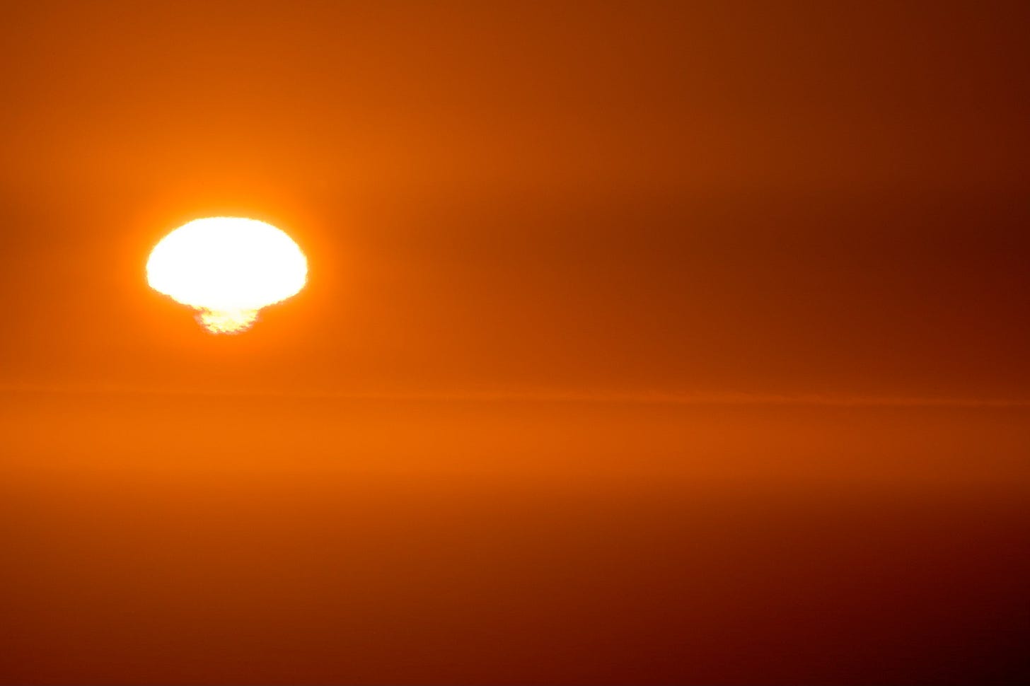 Orange sunset on the Pacific Ocean with the sun shape getting distorted by the atmosphere.
