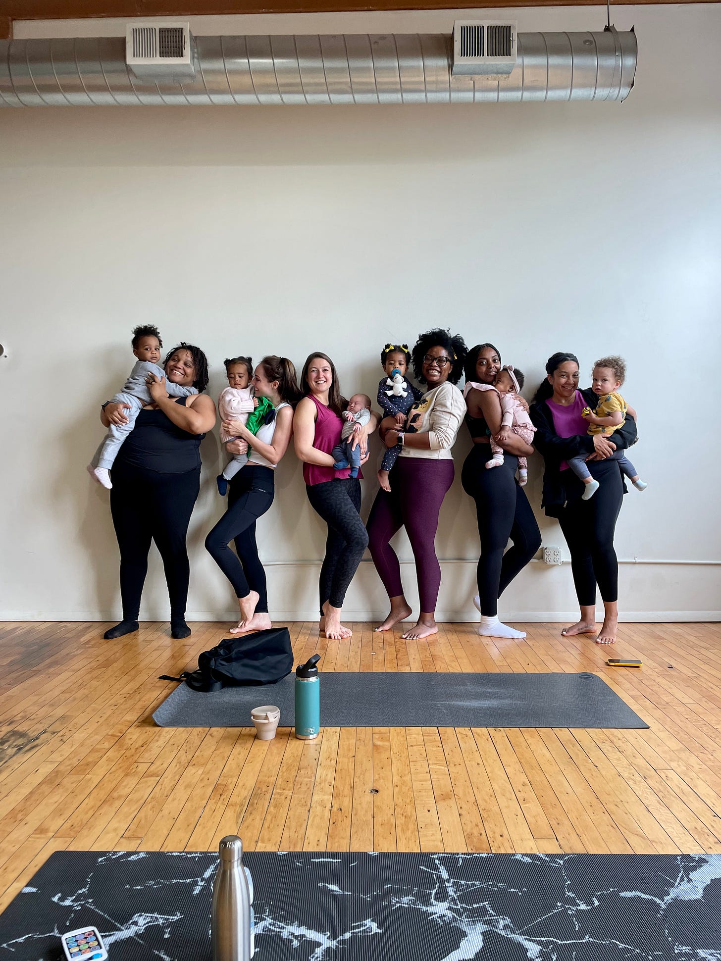 Multicultural group of moms holding their children with yoga mats in the forefront of the picture