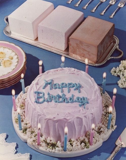 This may contain: a birthday cake with candles on it sitting in front of other plates and silverware
