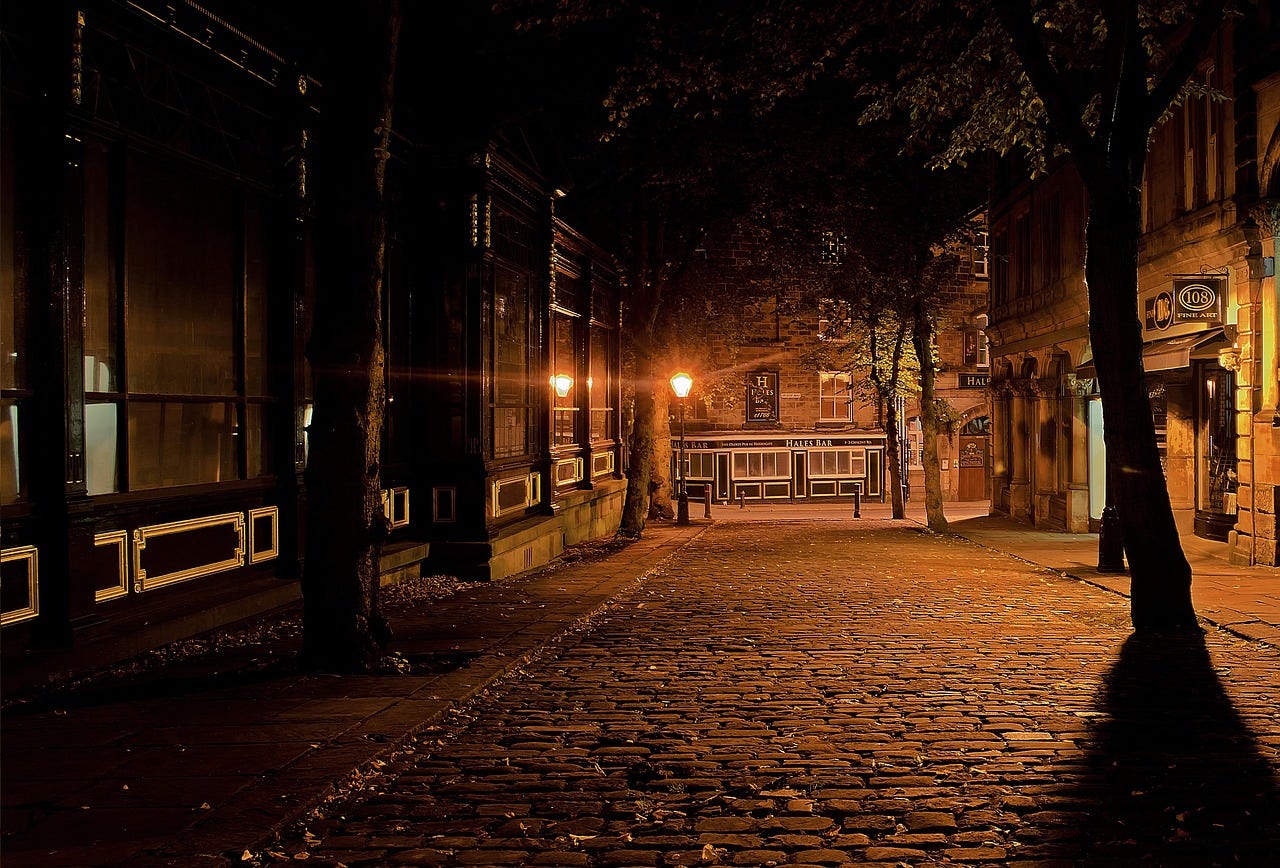 A cobblestone street at night, lit by streetlights, with long shadows everywhere A cobblestone street at night, lit by streetlights, with long shadows everywhere