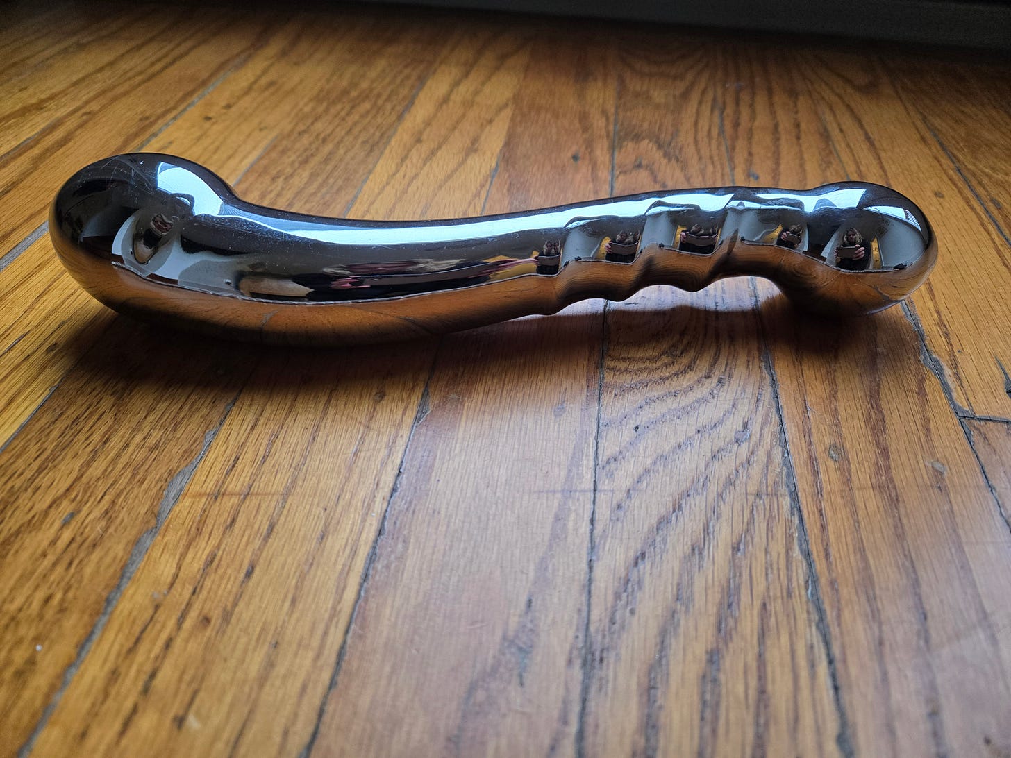 eleven large curved shiny silver colored metal dildo on a wood floor eleven large curved shiny silver colored metal dildo on a wood floor