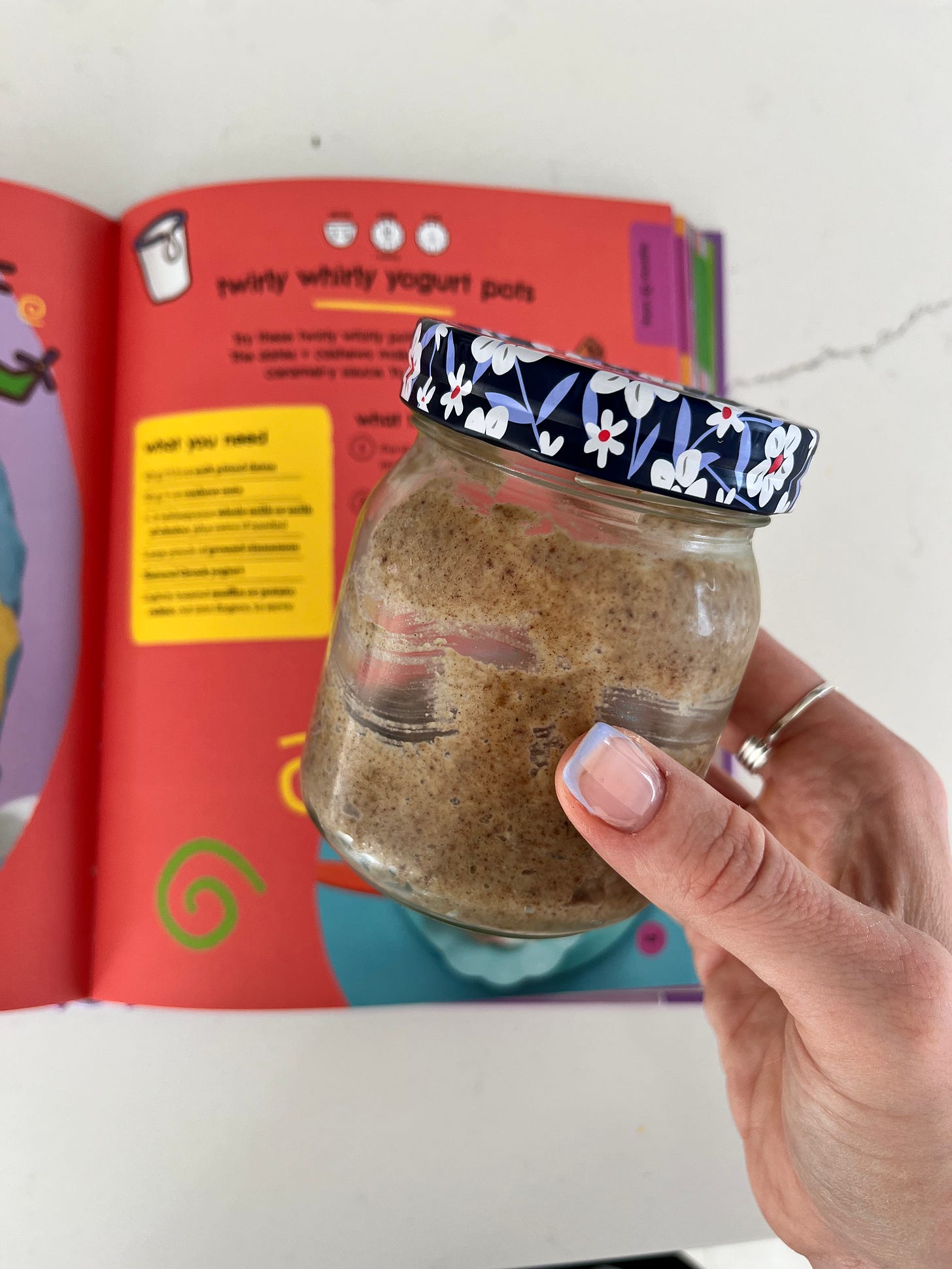 A jar of homemade date paste against a background of a recipe page that is red. A jar of homemade date paste against a background of a recipe page that is red.