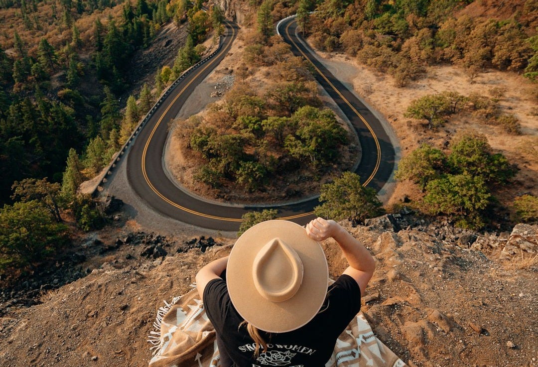person in black and white long sleeve shirt and beige cowboy hat sitting on brown rock