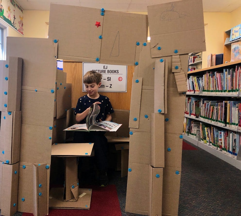 A kid is reading in a cardboard castle in the library.