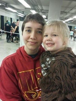 Young woman with short brown hair and a red sweatshirt holding her blonde haired toddler