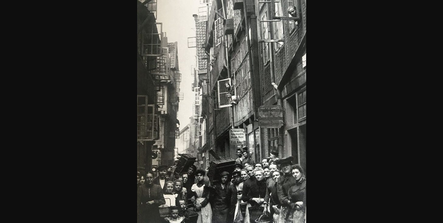 a photo of the 19th century slums in hamburg, showing very tall buildings in a very narrow street, with a crowd of people in front of the camera