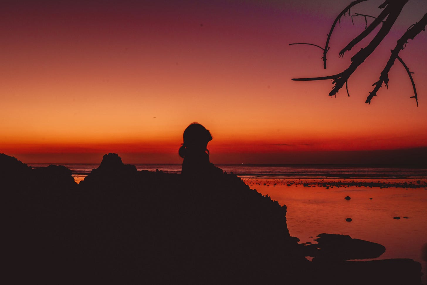a-silhouette-of-a-person-sitting-on-a-rock-at-sunset