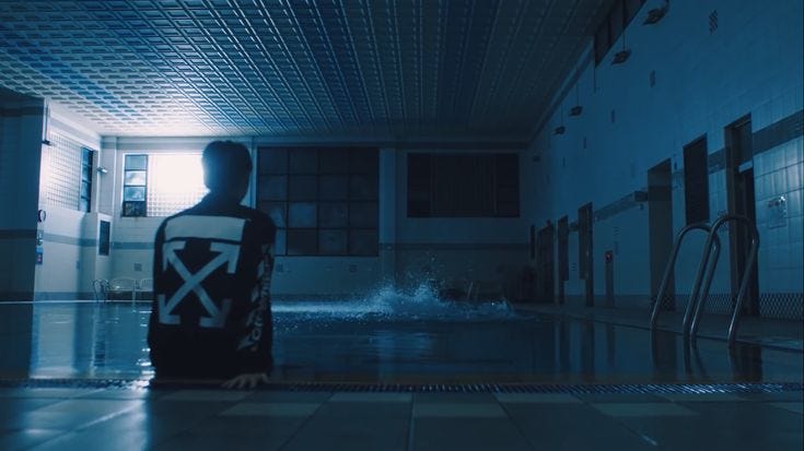 This may contain: a man sitting on the side of a swimming pool, watching 4 of his friends messing around in the water