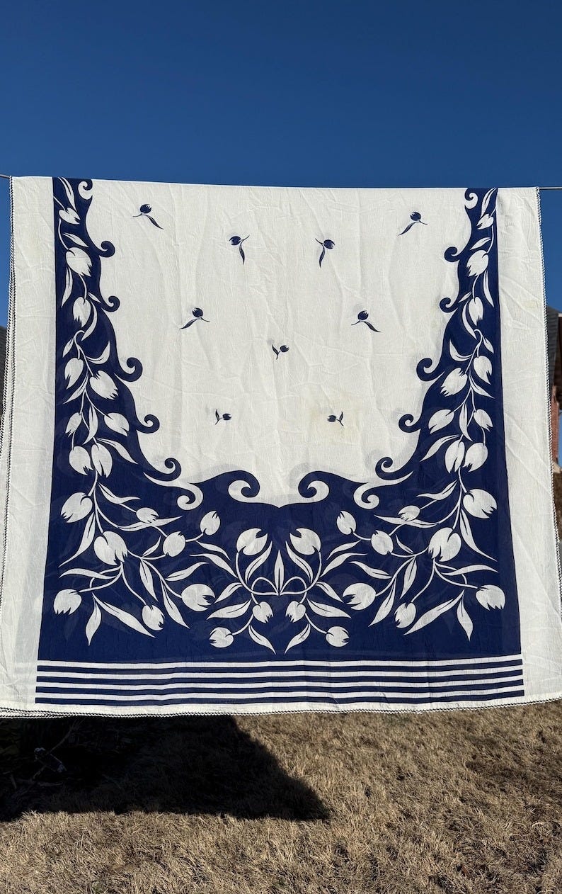 May include: White tablecloth with a blue floral border. The border features a repeating pattern of stylized tulips and leaves. The tablecloth has a white background with a blue floral border.