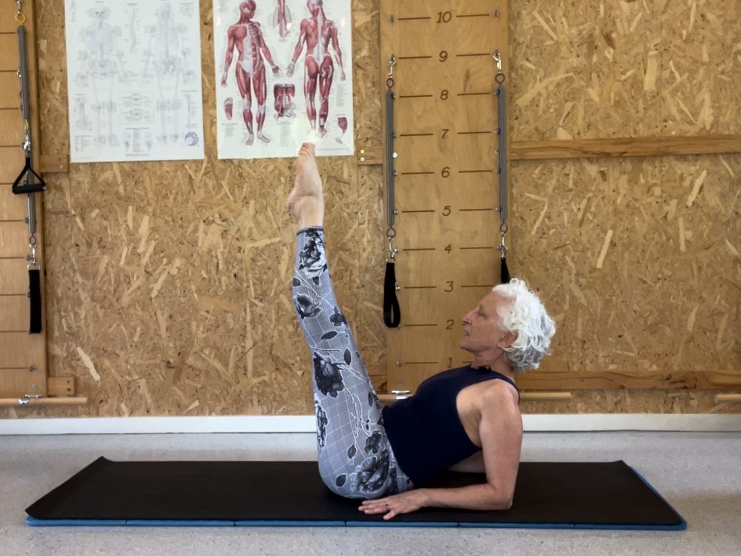 woman on Pilates mat, leaning back on elbows with legs up in air