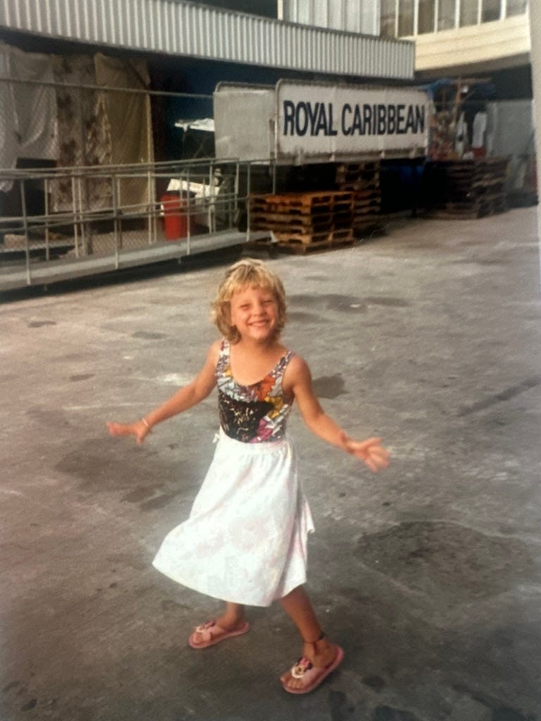 Girl twirling on the asphalt in front of a Royal Caribbean sign.