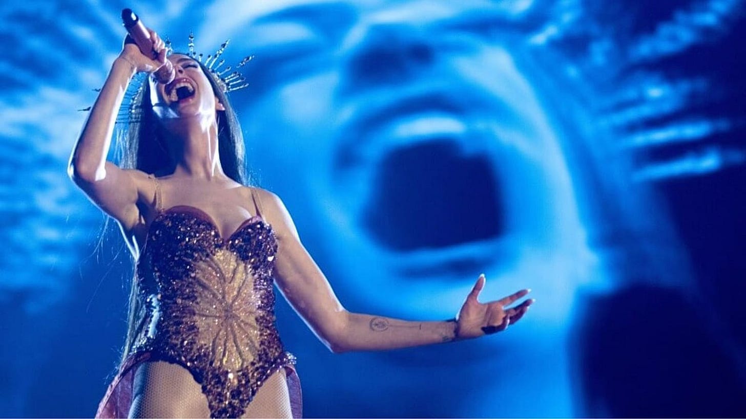 Movie still from Mother Mary. Mary performs on stage, her own image on the screen behind her.