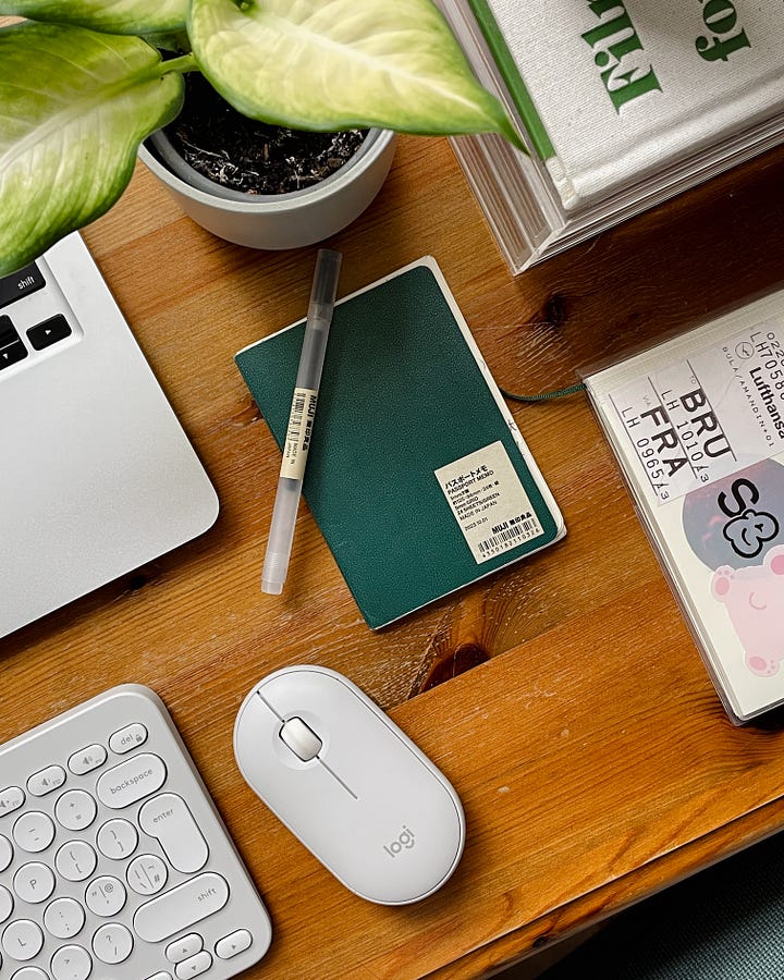 Gallery - Image 1: A close-up of my laptop and cup of coffee on my desk. / Image 2: A close-up of my Muji passport notebook, plant, laptop, and desk accessories.