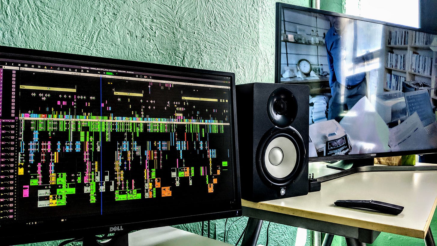 a computer monitor with a timeline, another monitor with the program in a room with a green stucco wall