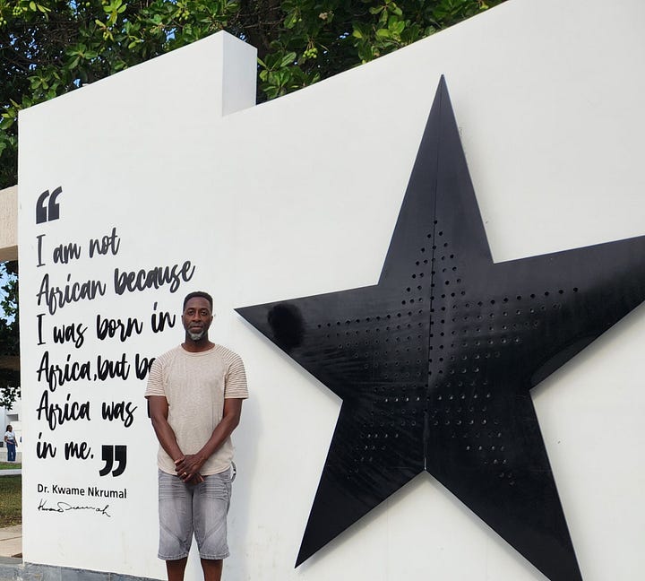 Nii Addy standing in front of a statue of Dr. Kwame Nkrumah. Nii Addy standing in front of a quote from Dr. Nkrumah, which reads "I am not African because I was born in Africa, but because Africa was born in me."