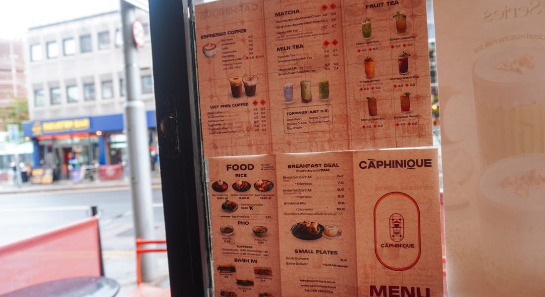 A window with a pink food menu on it, with a street behind it