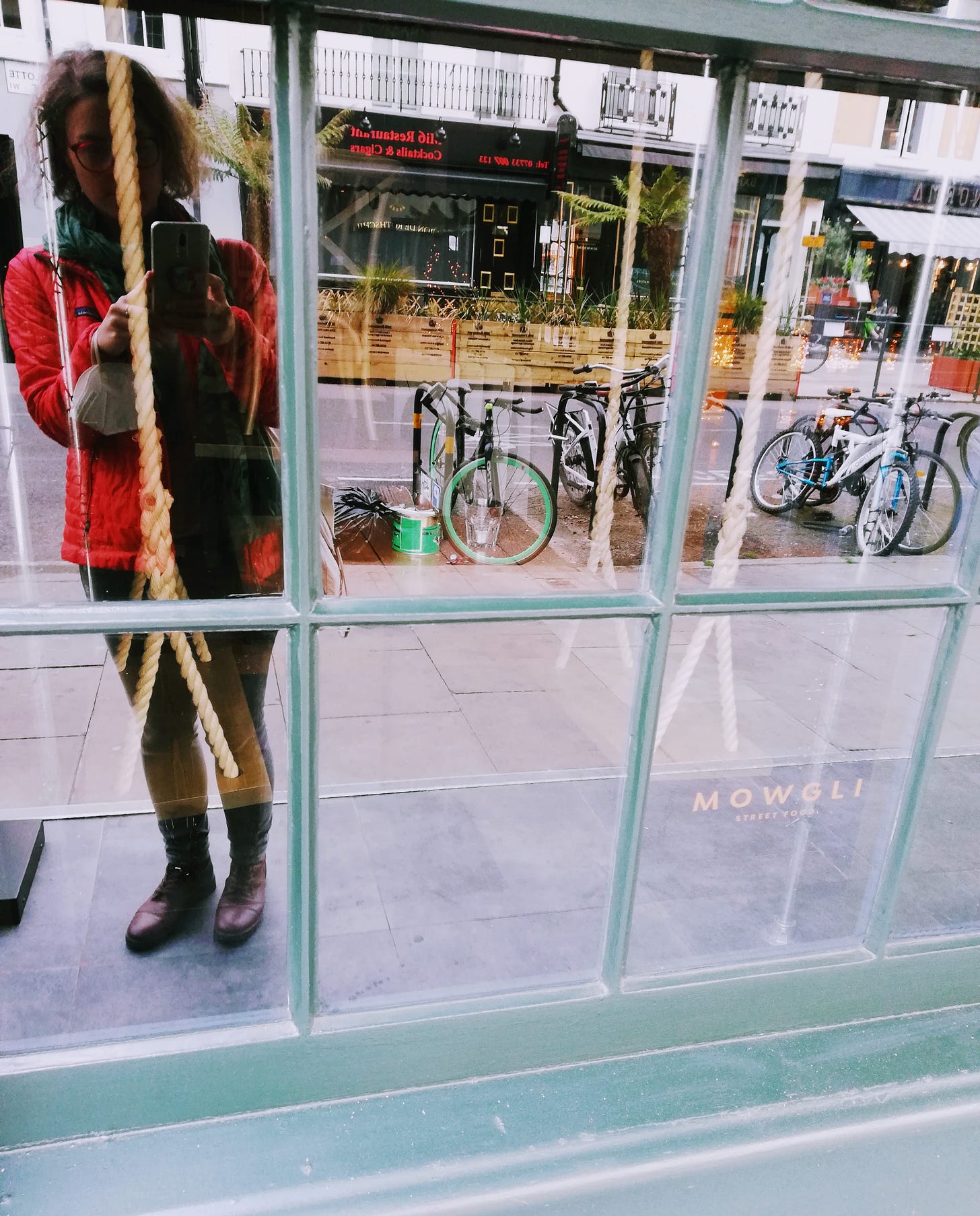 The brown-haired woman is standing in front of a window, taking a selfie in London in April 2022. Six weeks later, she had Covid-19. There are bikes and buildings. The moment carries a mask visibly on her. The brown-haired woman is standing in front of a window, taking a selfie in London in April 2022. Six weeks later, she had Covid-19. There are bikes and buildings. The moment carries a mask visibly on her.