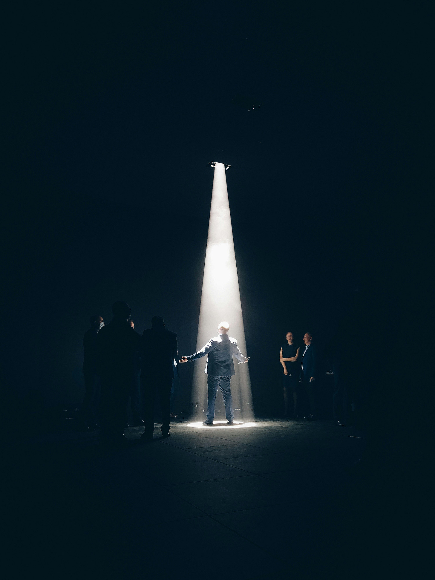 Mand on the center stage with arms with open while a bright light shines onto him.
