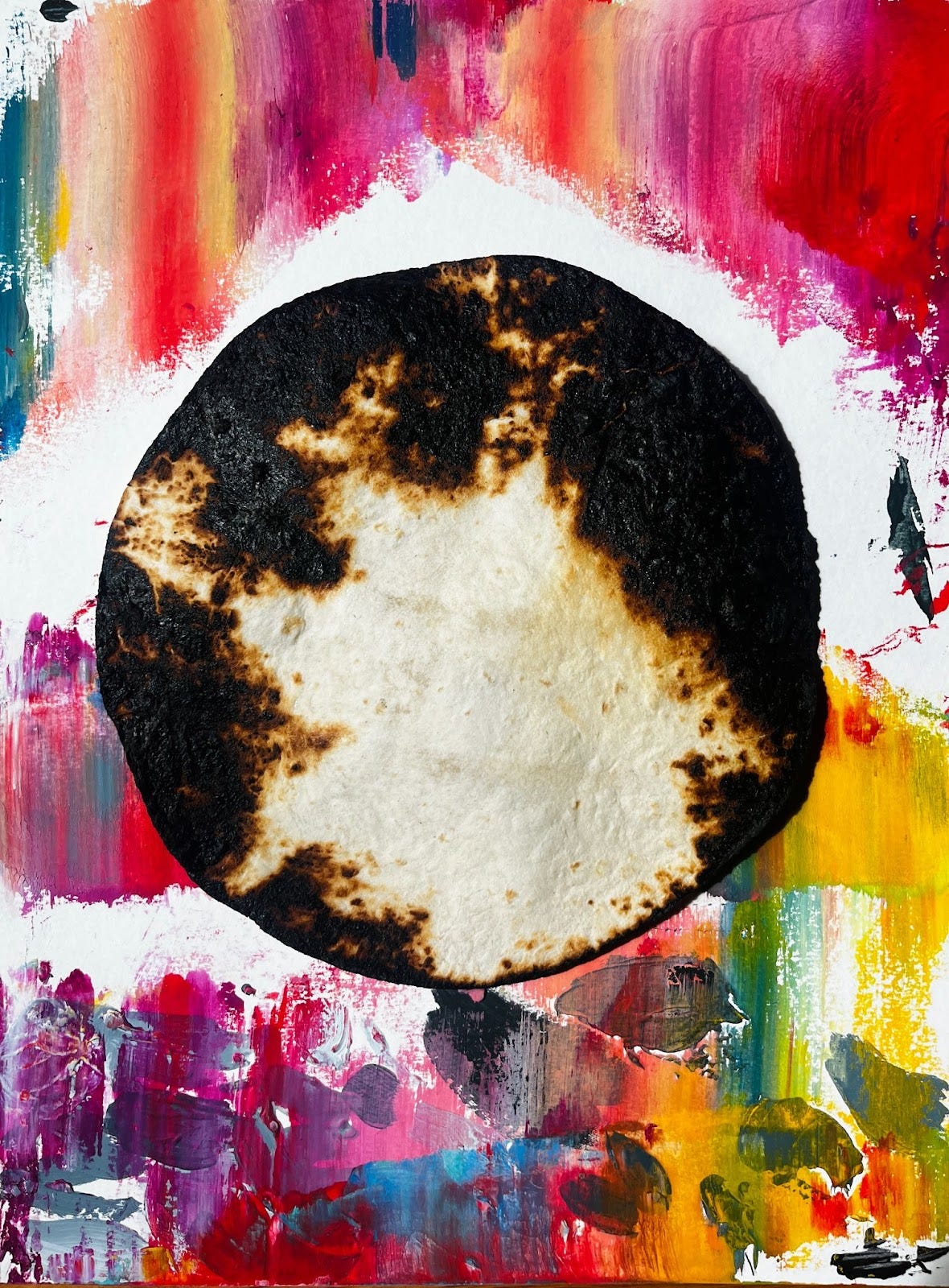 A photo of a charred tortilla with black edges on top of a colorful painted background