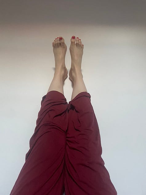 Image 1: Laura in side crow pose with split legs on a blue yoga matt outside on red pavers. Image 2: Black and white image of Laura outside on pavers in child's pose, a brick wall and sliding door in background. Image 3: Laura wearing colourful yoga pants in half lift, outside with a while mug at the top of her blue mat. Image 4: Laura in bambook pose in low light before sunrise in side, a wooden chair and rocking chair in the background. Image 5: Laura sitting on her blue yoga mat patting her white bun Percy on floating floors. Image 6: Laura in red pj pants with legs up the wall.