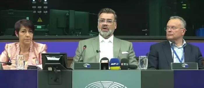 A person in a suit at a podium with microphones

AI-generated content may be incorrect.
