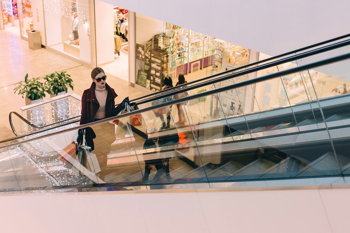 A woman rides an escalator in a shopping mall carrying multiple bags, reflecting consumer spending habits. Photo by Freestocks on Unsplash