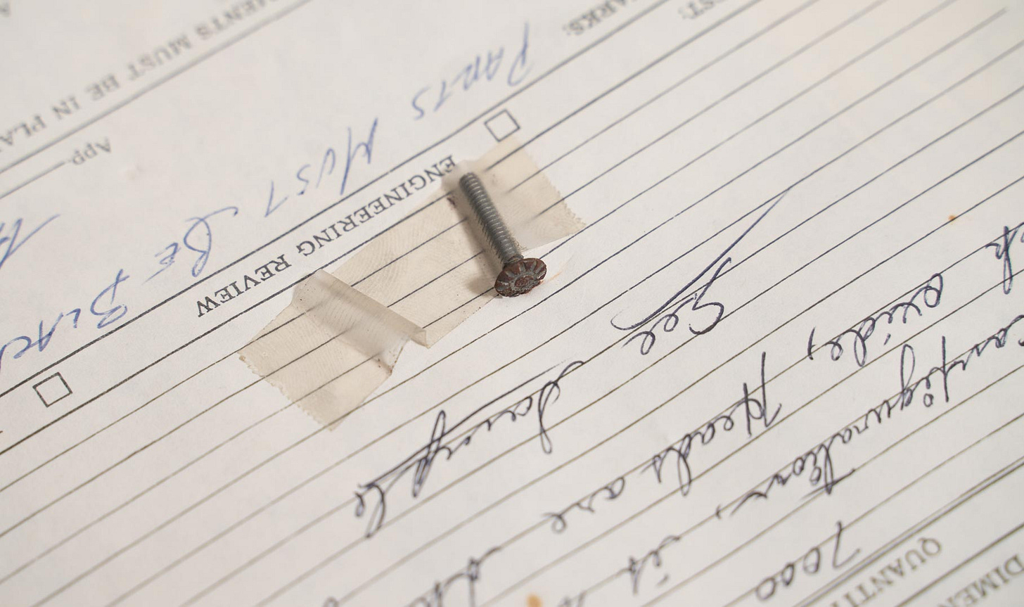 A closeup of the screw that is taped to the Quality Report in the previous image, showing the screwhead.