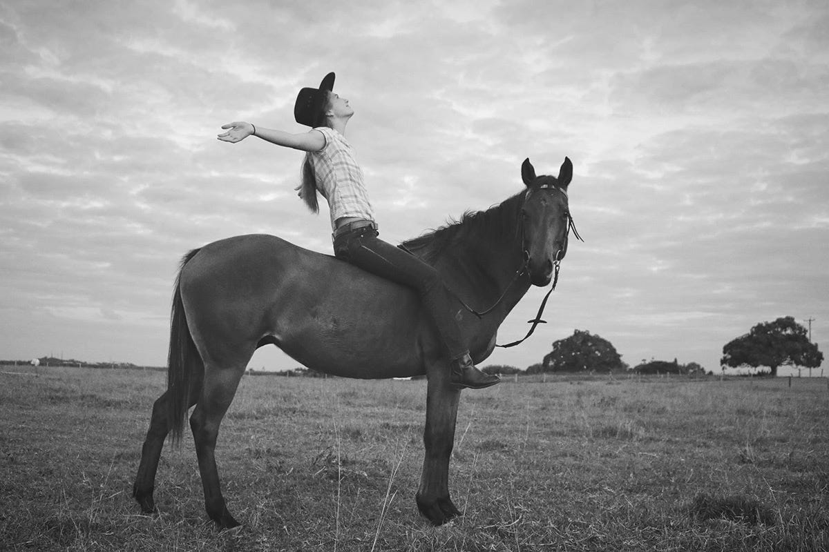 Femme assise sans selle sur un cheval, les bras ouverts et le regard tourné vers le ciel.
