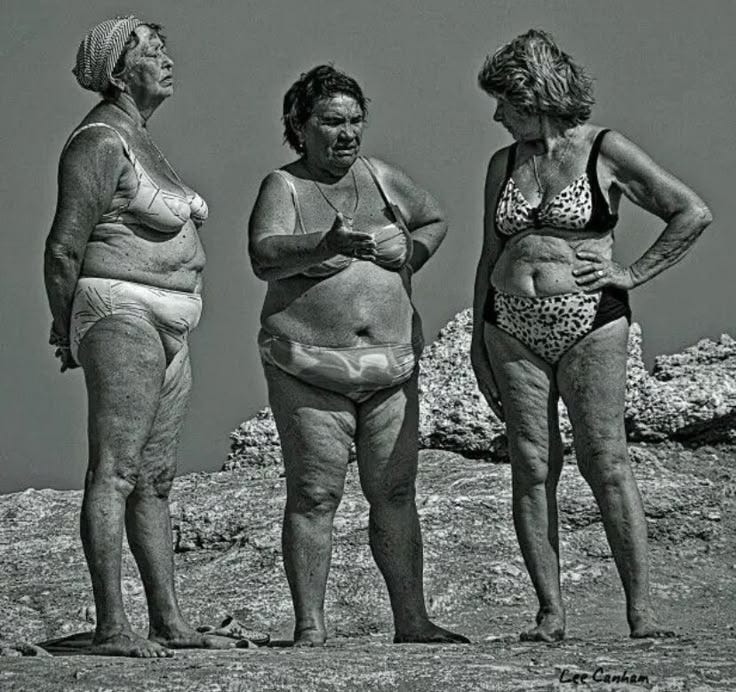 This may contain: three women in bathing suits standing next to each other on a rocky area with grass and rocks