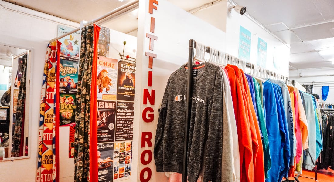 A fitting room with colourful changing rooms and a rail of colourful jumpers next to them