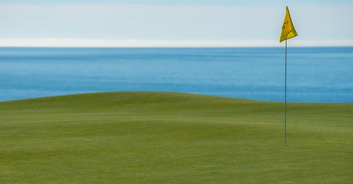 Photo: Anthony / Pexels Peaceful golf course by the ocean with a putting green and a flag under clear blue skies.
