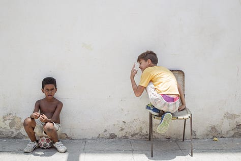 A 3x3 grid of nine photographs depicting life in Cuba. Images include: a boy diving into water; children sitting by a wall; flamingos in a lake; colorful colonial street scenes with classic cars and horse-drawn carts; a cat and a dog in a window; and a lamp-lit cobblestone street at night.