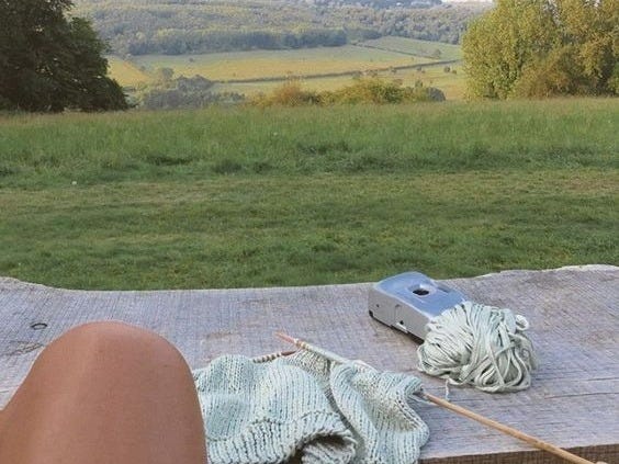 This may contain: a person's feet resting on a picnic table with a book and knitting needle This may contain: a person's feet resting on a picnic table with a book and knitting needle